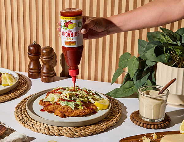 A caesar salad crispy chicken cutlet topped with Yuzu Sriracha.