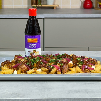 A pork belly recipe on a sheet tray, glazed in hoisin, and served on top of a poutine.