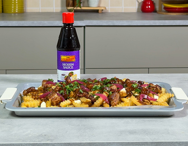 A pork belly recipe on a sheet tray, glazed in hoisin, and served on top of a poutine.