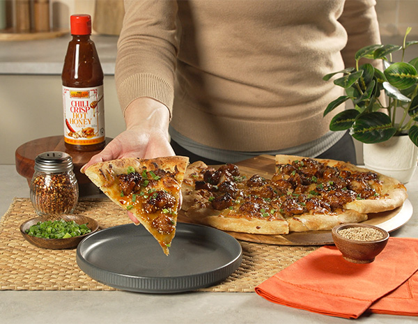 An orange chicken pizza recipe served with chili crisp hot honey.