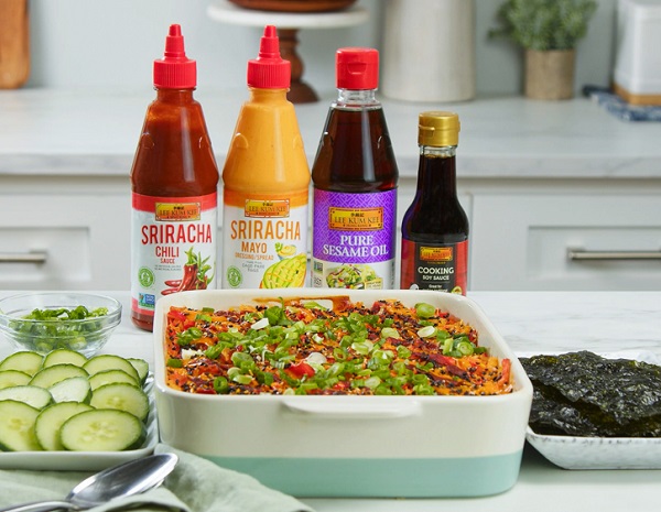 An ceramic baking dish containing a fully cooked spicy sushi bake casserole with imitation crab, surrounded by toppings and LKK sauces