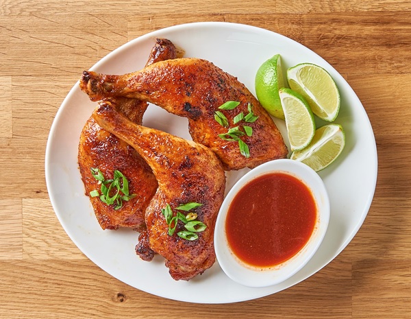 Honey sriracha chicken legs from the air fryer on a serving platter, alongside Lee Kum Kee Sriracha and limes