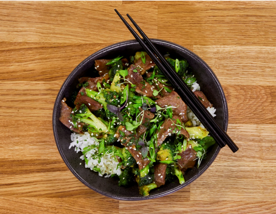 Beef and Broccoli Stir Fry topping a bowl of rice on a wooden table surface