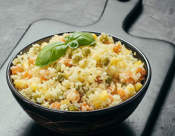 Cauliflower Fried Rice in a black bowl on top of a black wooden cutting board