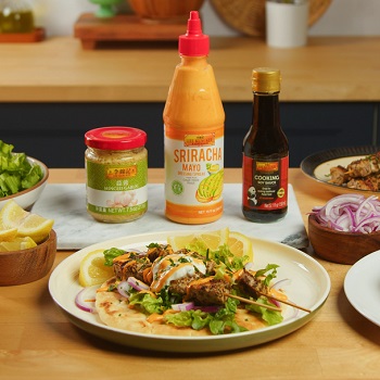 A plate of pork souvlaki skewers from Lee Kum Kee’s recipe using Lee Kum Kee Minced Garlic, Sriracha Mayo, and Cooking Soy Sauce in the background with various ingredients