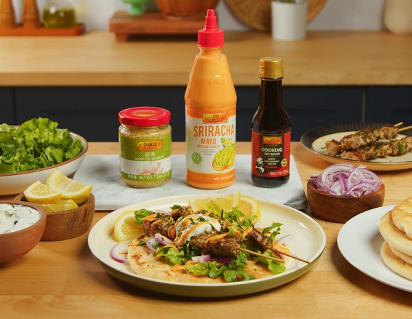 A plate of pork souvlaki skewers from Lee Kum Kee’s recipe using Lee Kum Kee Minced Garlic, Sriracha Mayo, and Cooking Soy Sauce in the background with various ingredients 