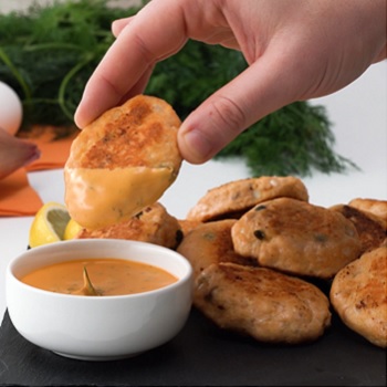 Hand dipping a salmon croquette into sriracha dill sauce, with several more simple salmon croquettes from Lee Kum Kee’s recipe