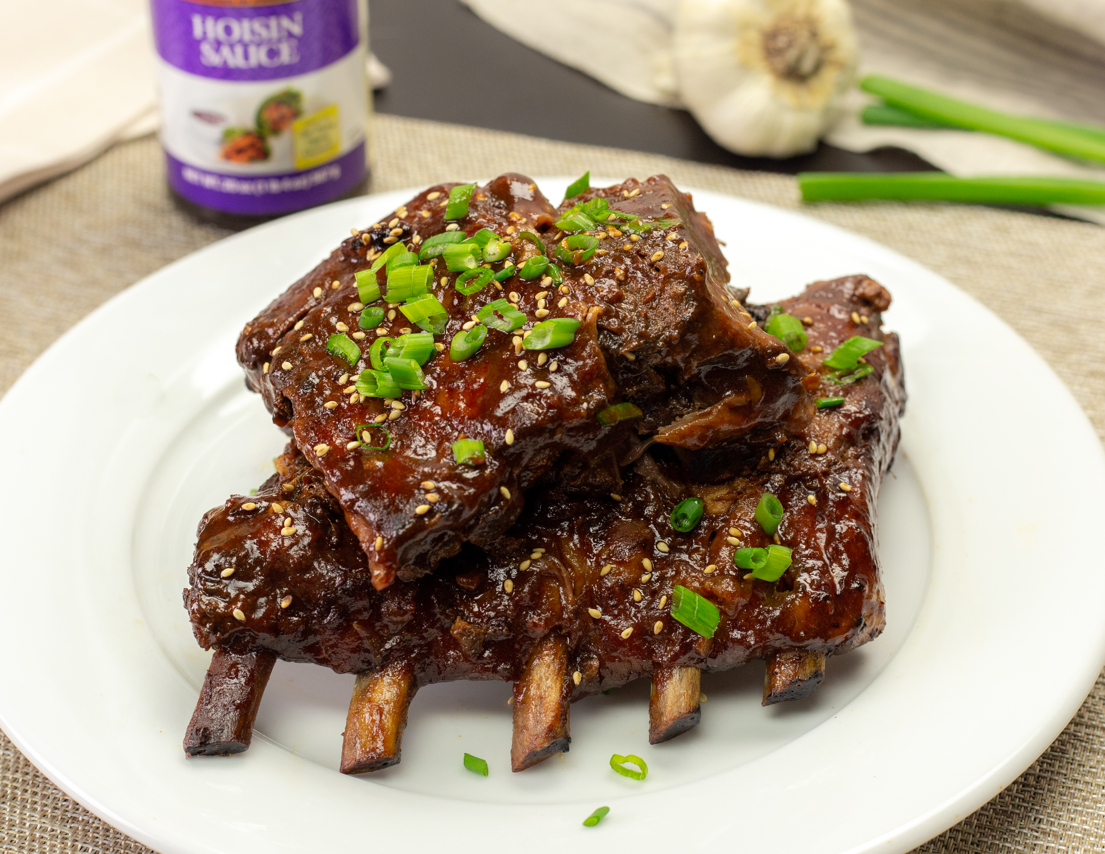 Slow Cooked Hoisin Pork Ribs on a white plate with ingredients in the background