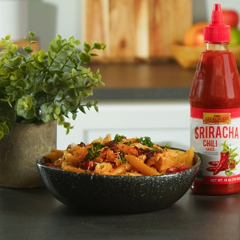 Spicy Cajun pasta in a serving bowl, alongside the Lee Kum Kee sriracha sauce used in the recipe