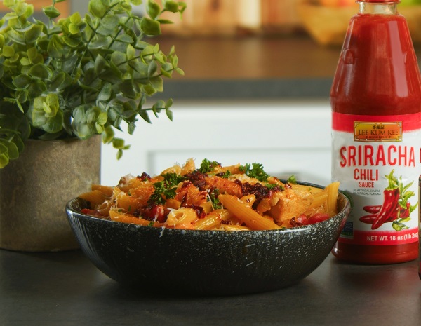 Spicy Cajun pasta in a serving bowl, alongside the Lee Kum Kee sriracha sauce used in the recipe