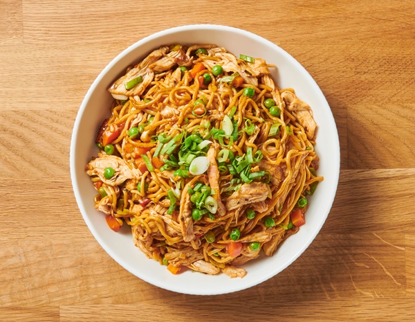 Stir-Fried Noodles with chicken in a white serving bowl on a wooden surface