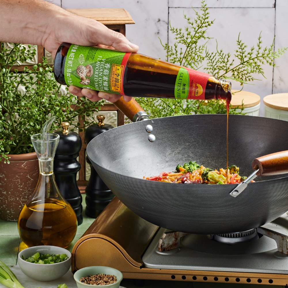 Lee Kum Kee vegan oyster sauce, aka vegetarian mushroom stir-fry-sauce, being added to a wok of chow mein noodles.