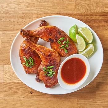 Honey sriracha chicken legs from the air fryer on a serving platter, alongside Lee Kum Kee Sriracha and limes