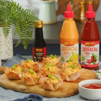 Crab rangoon cups on a serving board, alongside the LKK sauces used in the dish