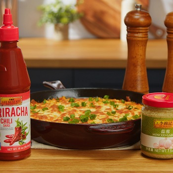 A heavy cast iron skillet containing prepared Korean-style cheese corn, surrounded by Lee Kum Kee ingredients